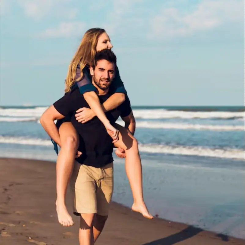 Pareja joven y feliz en la playa, hombre llevando a una mujer en la espalda frente al mar en un día soleado